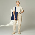 WharfPrint deep navy cotton canvas tote bag carried by a model wearing a beige t-shirt and matching sweatpants.